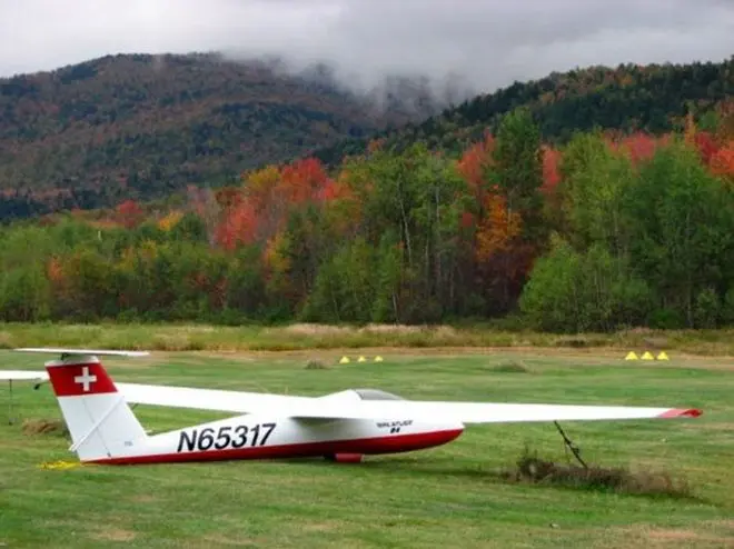 A white and red glider parked on the grass at the airfield