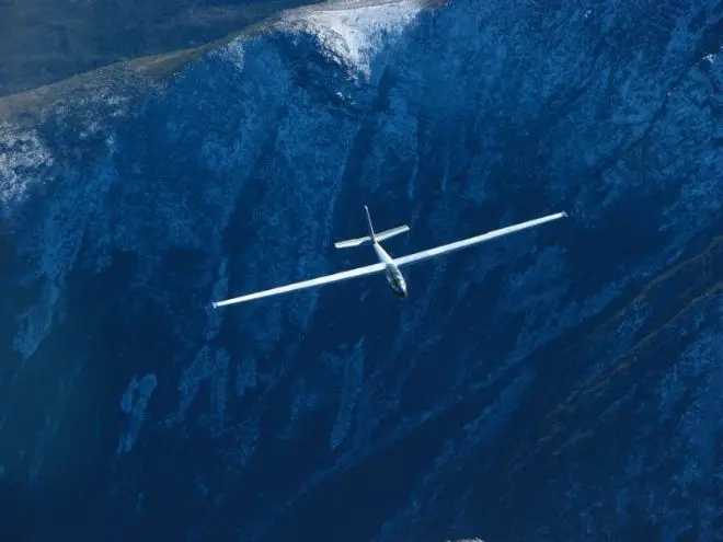 A glider soaring over a dark ridge in the White Mountains
