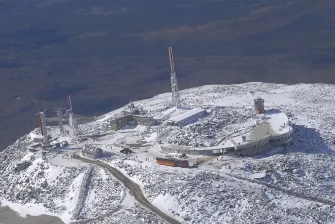 Aerial view of the snow-covered Mount Washington summit and its observatory