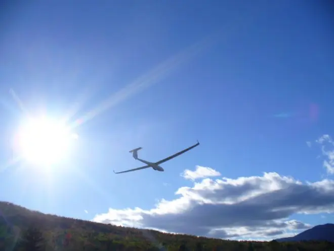 A glider silhouetted against the sun above a wooded ridge