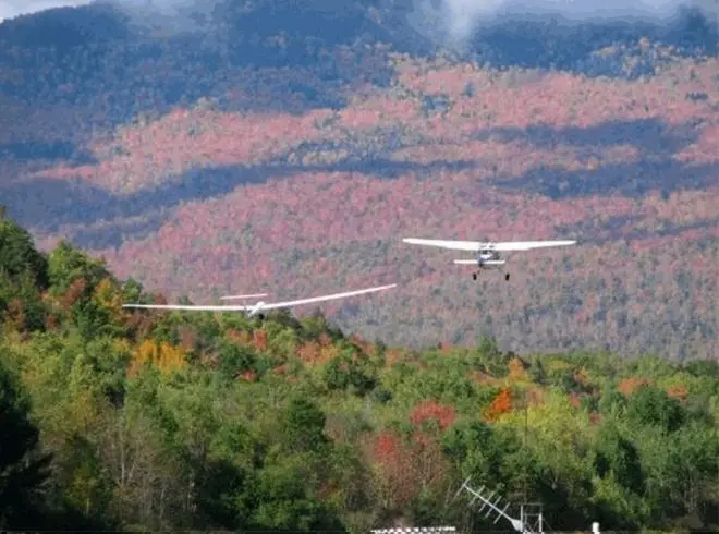 A tow plane pulling a glider over autumn mountains